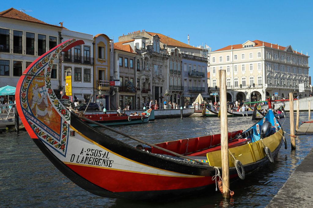 A traditional painted wooden boat is moored on a canal lined with historic buildings under a clear blue sky.
