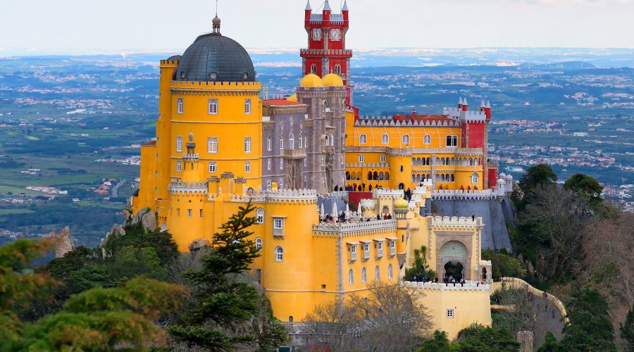 Pena Palace, a colorful 19th-century Romanticist castle, stands on a hilltop surrounded by trees, overlooking the landscape of Sintra, Portugal. Pena Palace, a colorful 19th-century Romanticist castle, stands on a hilltop surrounded by trees, overlooking the landscape of Sintra, Portugal.