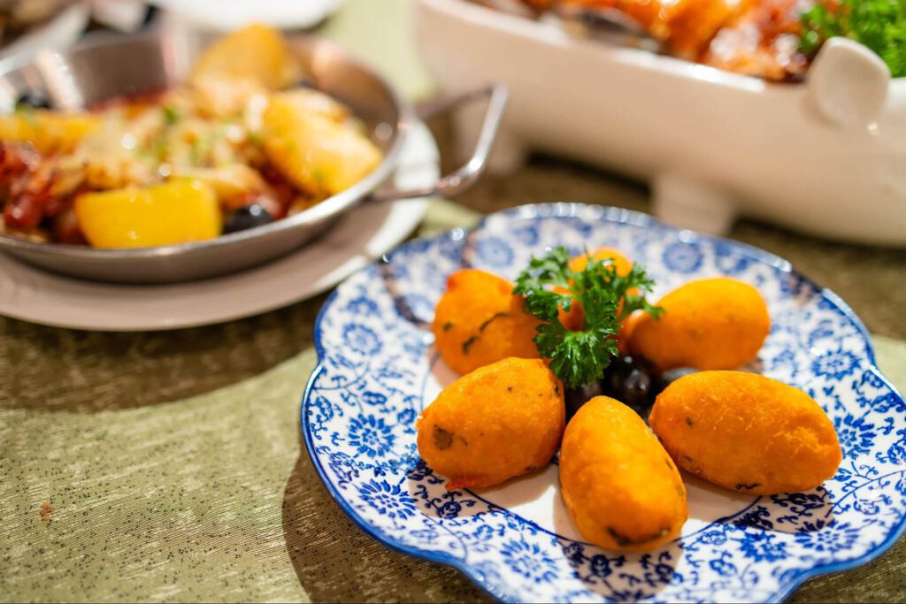 A blue and white plate holds six oval-shaped, golden fried appetizers garnished with parsley—a must-try for any first-time visitor seeking authentic flavors, with another dish blurred in the background.