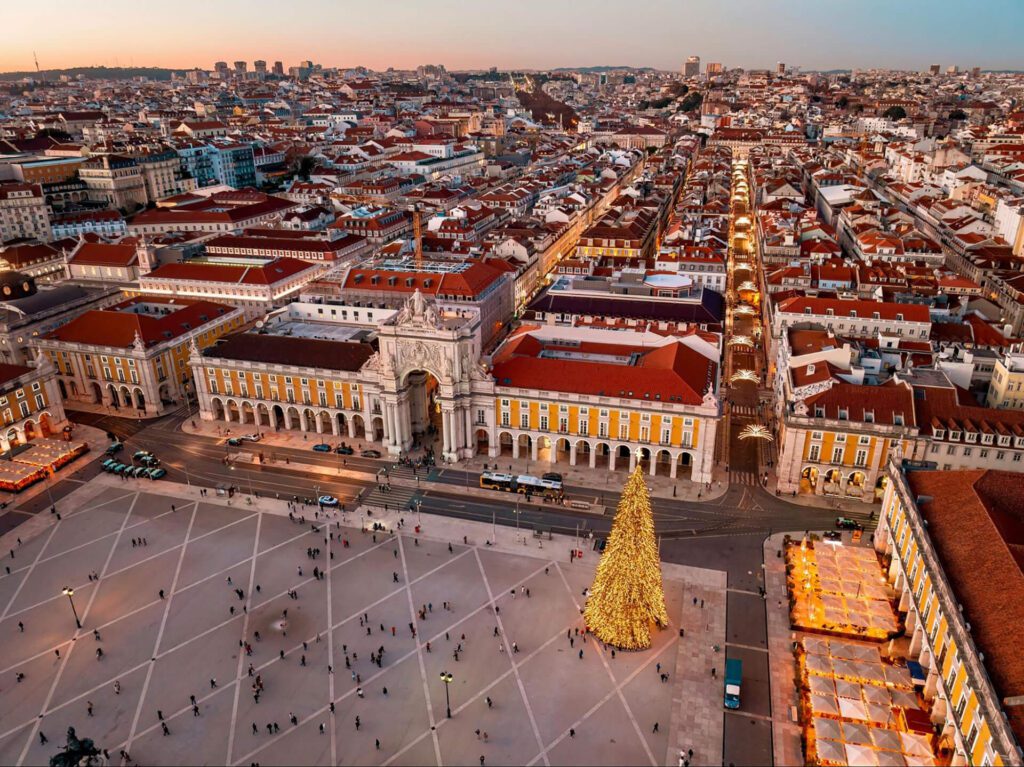 Aerial view of a large city square with a decorated Christmas tree, historic buildings, and festive lights at sunset—a magical scene often featured in Portugal travel guides as the best time to visit Portugal during the holiday season.