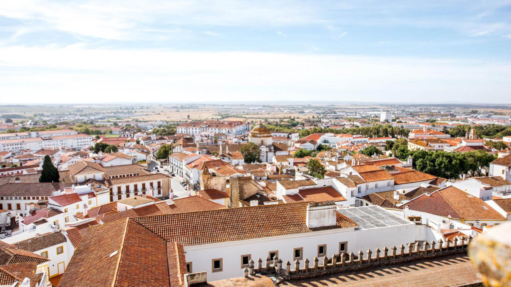 A panoramic view of a town with white buildings and terracotta roofs, surrounded by fields under a blue sky—one of the hidden gems Portugal offers to those seeking underrated places in Portugal.