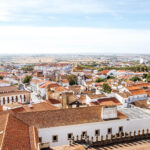 A panoramic view of a town with white buildings and terracotta roofs, surrounded by fields under a blue sky—one of the hidden gems Portugal offers to those seeking underrated places in Portugal.