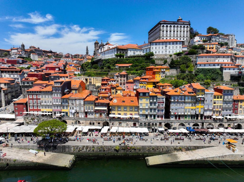 Aerial view of colourful buildings along the Douro River in Porto, Portugal, with historic hillside structures under a clear blue sky—a highlight on any best Portugal itinerary.