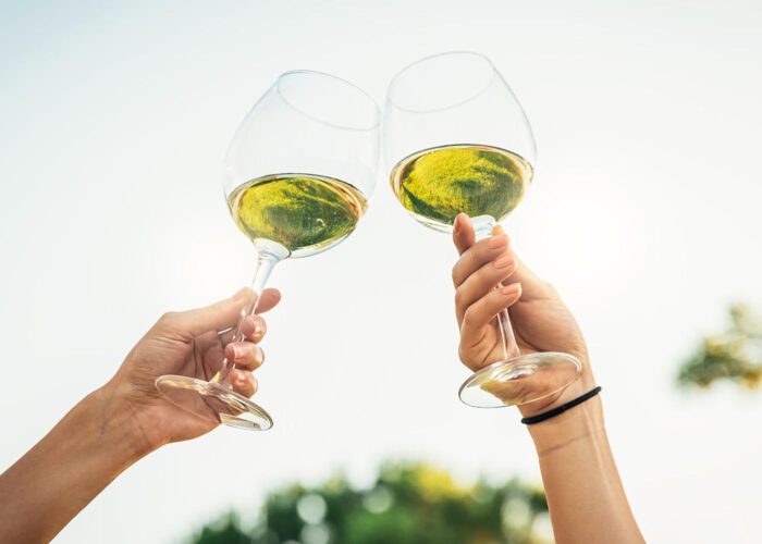 Two hands clinking wine glasses filled with Portuguese wine outdoors against a bright sky.