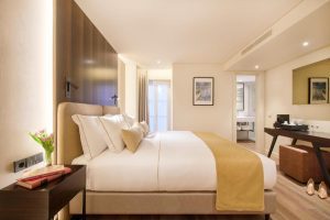 Modern hotel room featured on our 8-Day Portugal Tour, with a neatly made double bed, yellow throw, desk with mirror, artwork on the walls, and a small vase of flowers on the bedside table.
