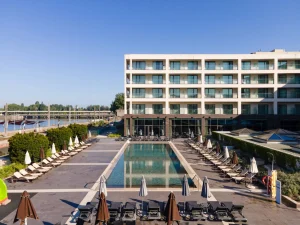A modern hotel with a central outdoor swimming pool, perfect for relaxing during your Portugal Explorer. Sun loungers and parasols await under a clear blue sky—a great stop on your 8-day Portugal tour.